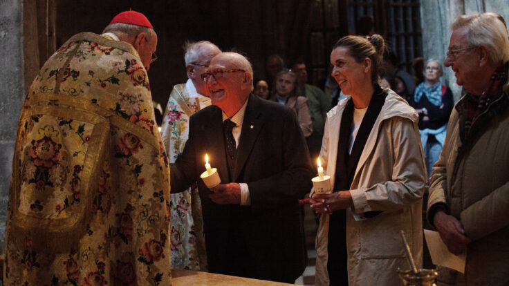 Kardinal Christoph Schönborn begrüßt Obmann Dr. Günter Geyer und die Vorstandsmitglieder Mag. Sonja Brandtmayer und Dr. Wolfgang Feuchtmüller. Dr. Geyer und Mag. Brandtmayer haben Festkerzen in den Händen. Kardinal und Obmann begrüßen einander herzlich.