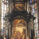 Zu sehen ist der obere Teil des Hochaltars flankiert von Buntglasfenstern.